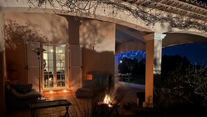 A covered patio area with outdoor seating, a fire feature, and a view of the night sky.