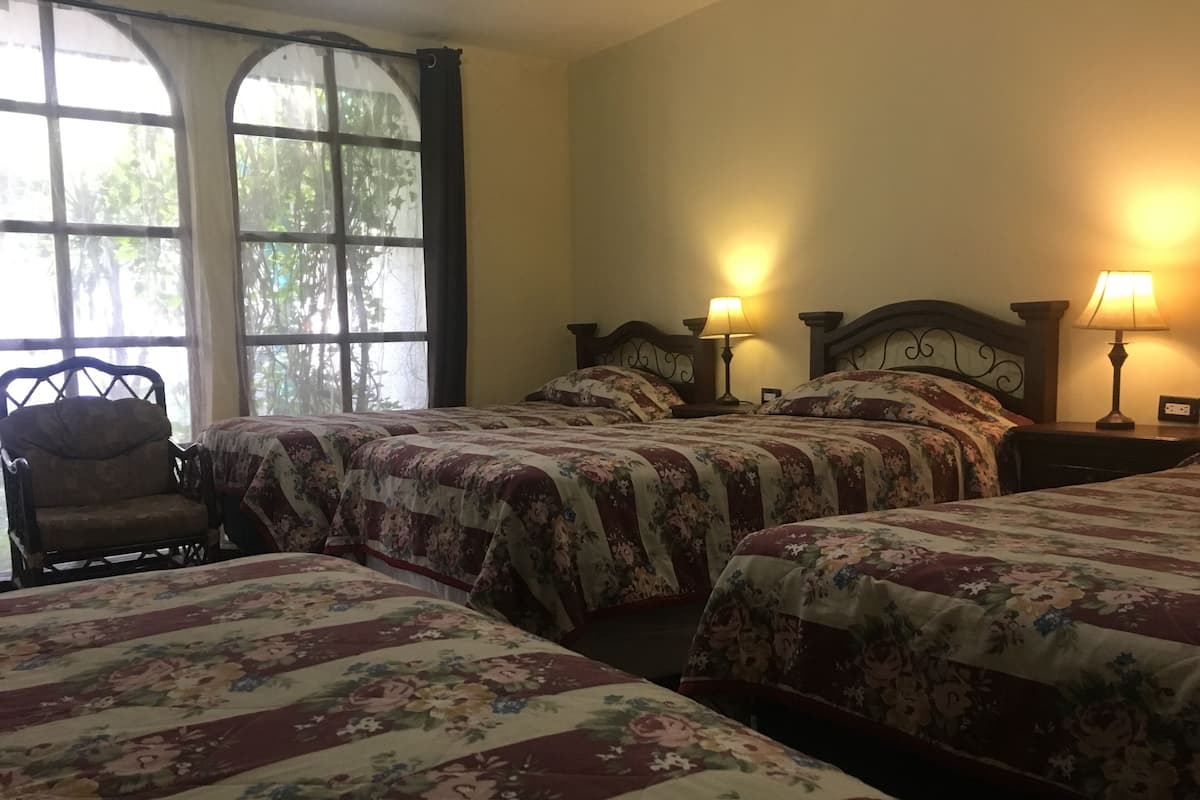 A room with three beds, each with floral bedding, a chair, and two bedside lamps.