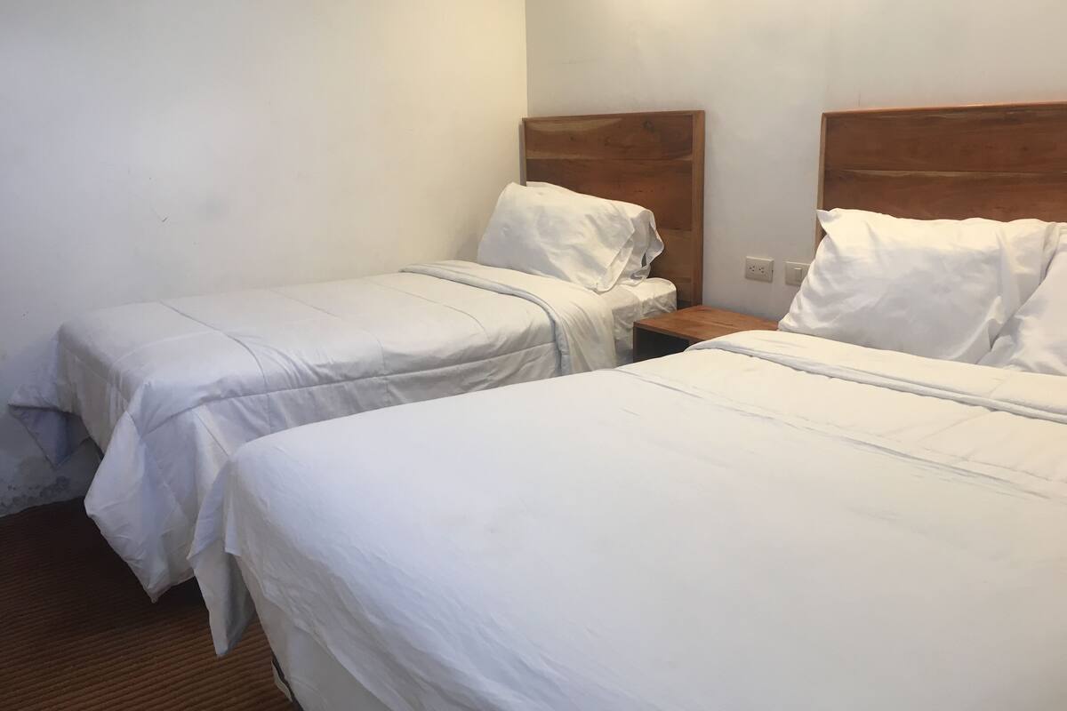 A hotel room with two single beds, a wooden headboard, a small wooden nightstand, and a white wall.