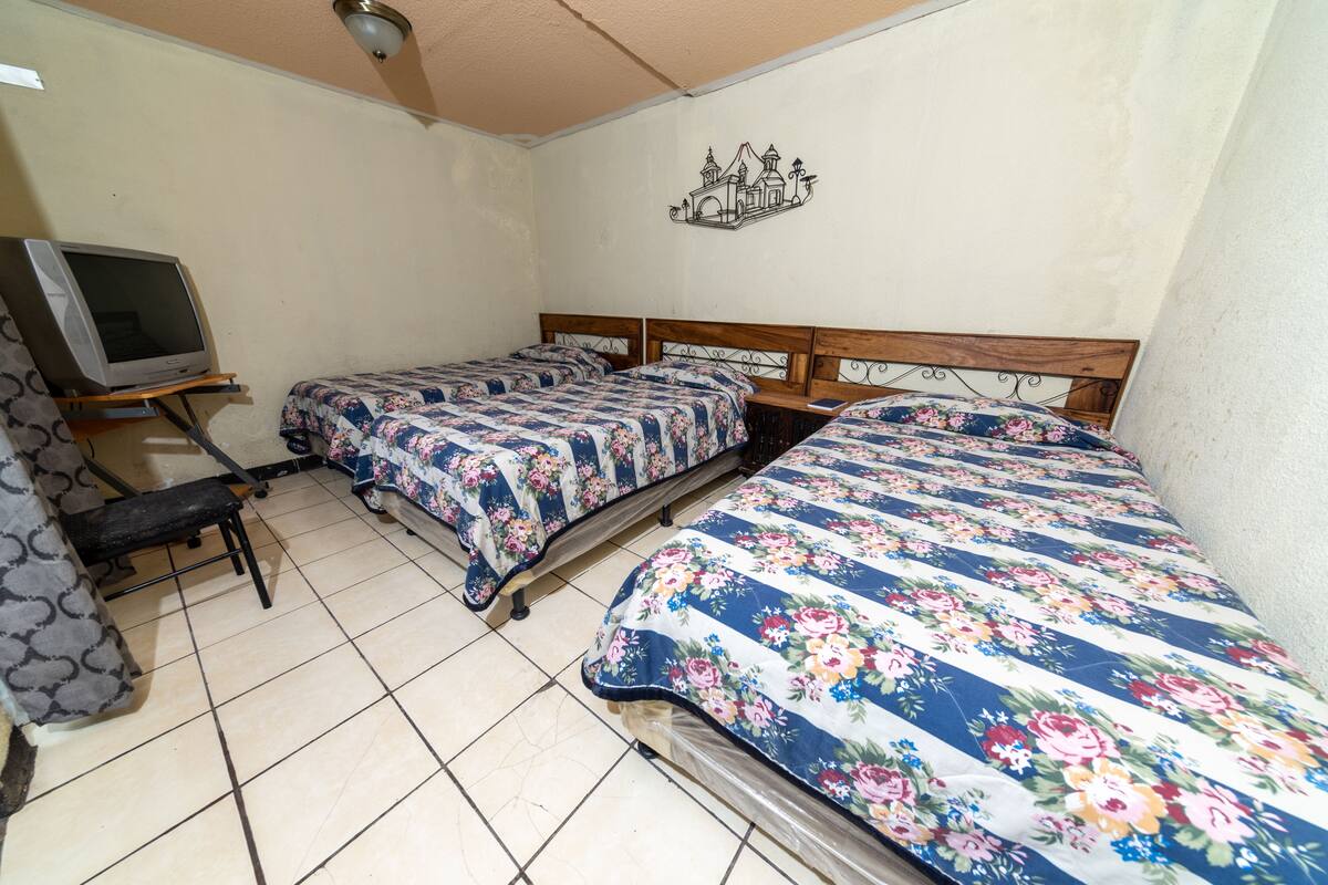 A room with three beds, a bench, and a television on a stand.