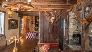 Ein rustikales Interieur mit Holzbalkendecke, einer Kristallleuchtre, einem Holztisch, einem rot gepolsterten Sessel und einem an der Wand befestigten Hirschkopf.