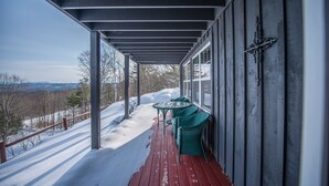 Ein überdachter Außenbereich mit Tisch und Stühlen, Schnee auf dem Boden und Blick auf Bäume und Berge.