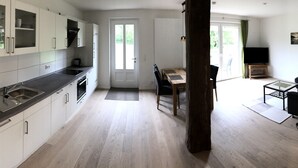 A modern kitchen with white cabinets, a black countertop, and a dining area with a wooden table and chairs. - Modern apartment in a quiet location for 4 persons (Brietlingen)