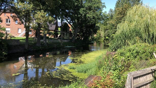 A serene riverside scene with a brick building, lush greenery, and a wooden fence. - Modern apartment in a quiet location for 4 persons (Brietlingen)