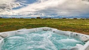 A hot tub with a panoramic view of a grassy field and distant mountains under a cloudy sky. - Wild Cat Cabin - Hot Tub - Foosball - Near Resort (Driggs)