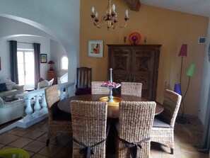 A dining area with wicker chairs, a round table, and a chandelier.