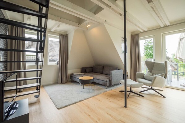 Relax in this spacious living area with a sofa, coffee table, and armchair, surrounded by a large window offering a view of the outdoors.