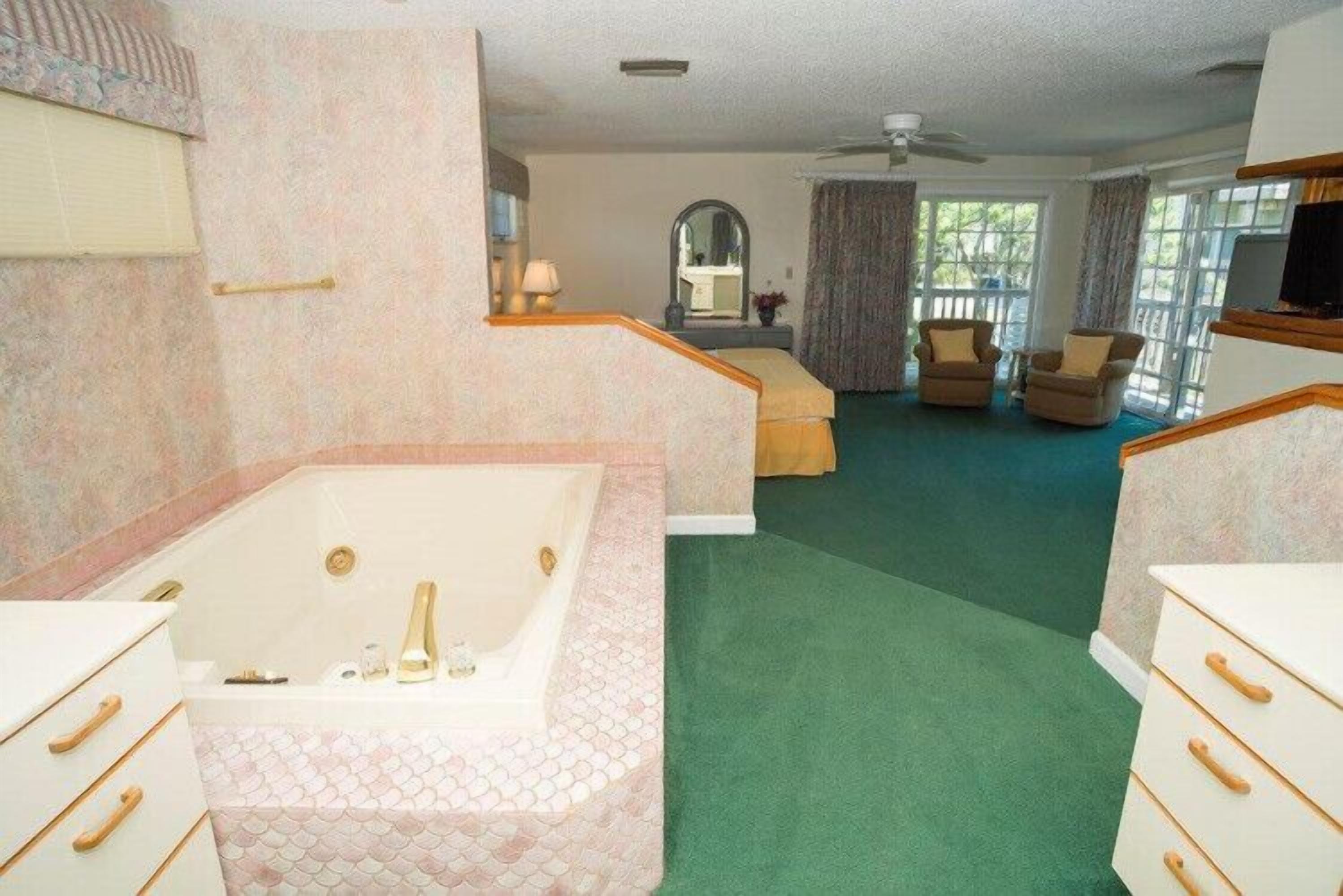 A hotel room with a large bathtub, a bed, a sitting area with a chair, and a television.