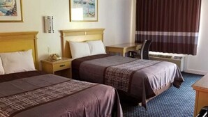 Ett hotellrum med två sängar, ett skrivbord, en stol och ett fönster med gardiner.