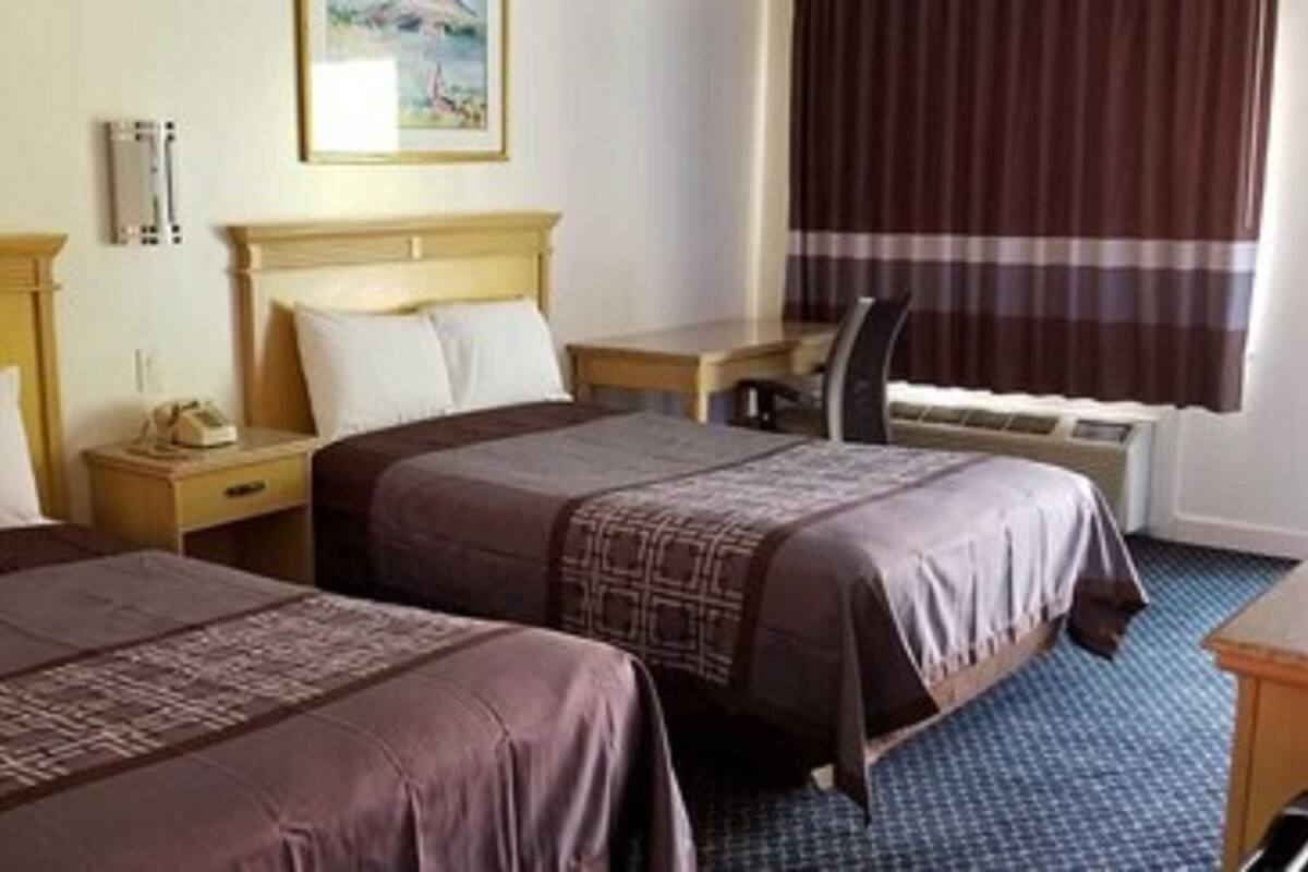 A hotel room with two beds, a desk, a chair, and a window with curtains.