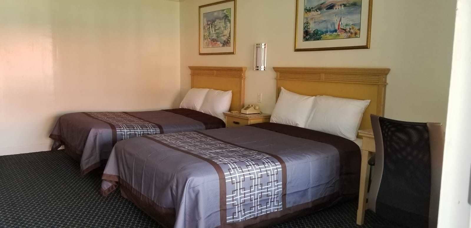 Ein Hotelzimmer mit zwei Betten, einem Nachttisch, einem Sessel und zwei Bildern an der Wand.
