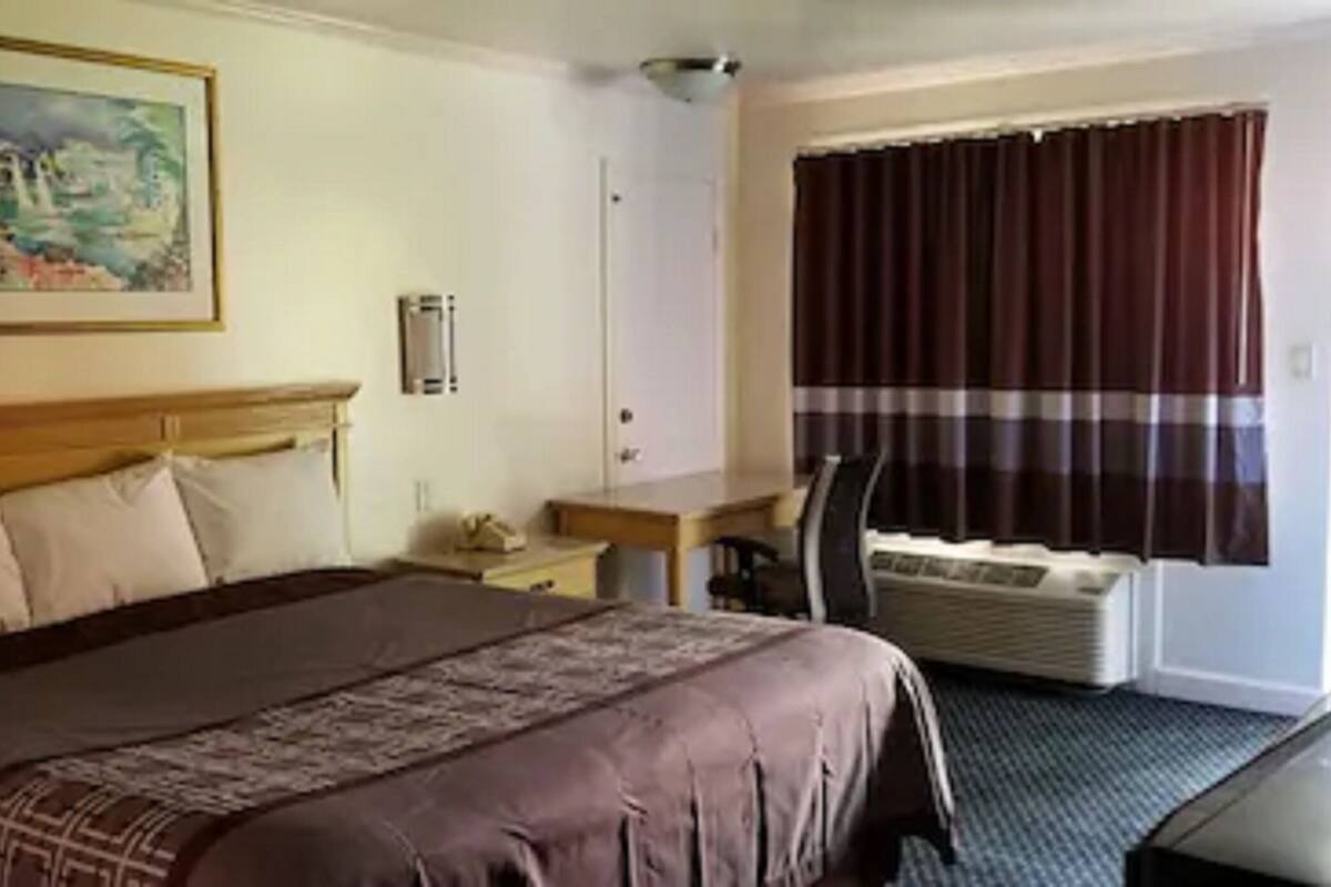 A hotel room with a large bed, a desk, a chair, a window with curtains, and a painting on the wall.