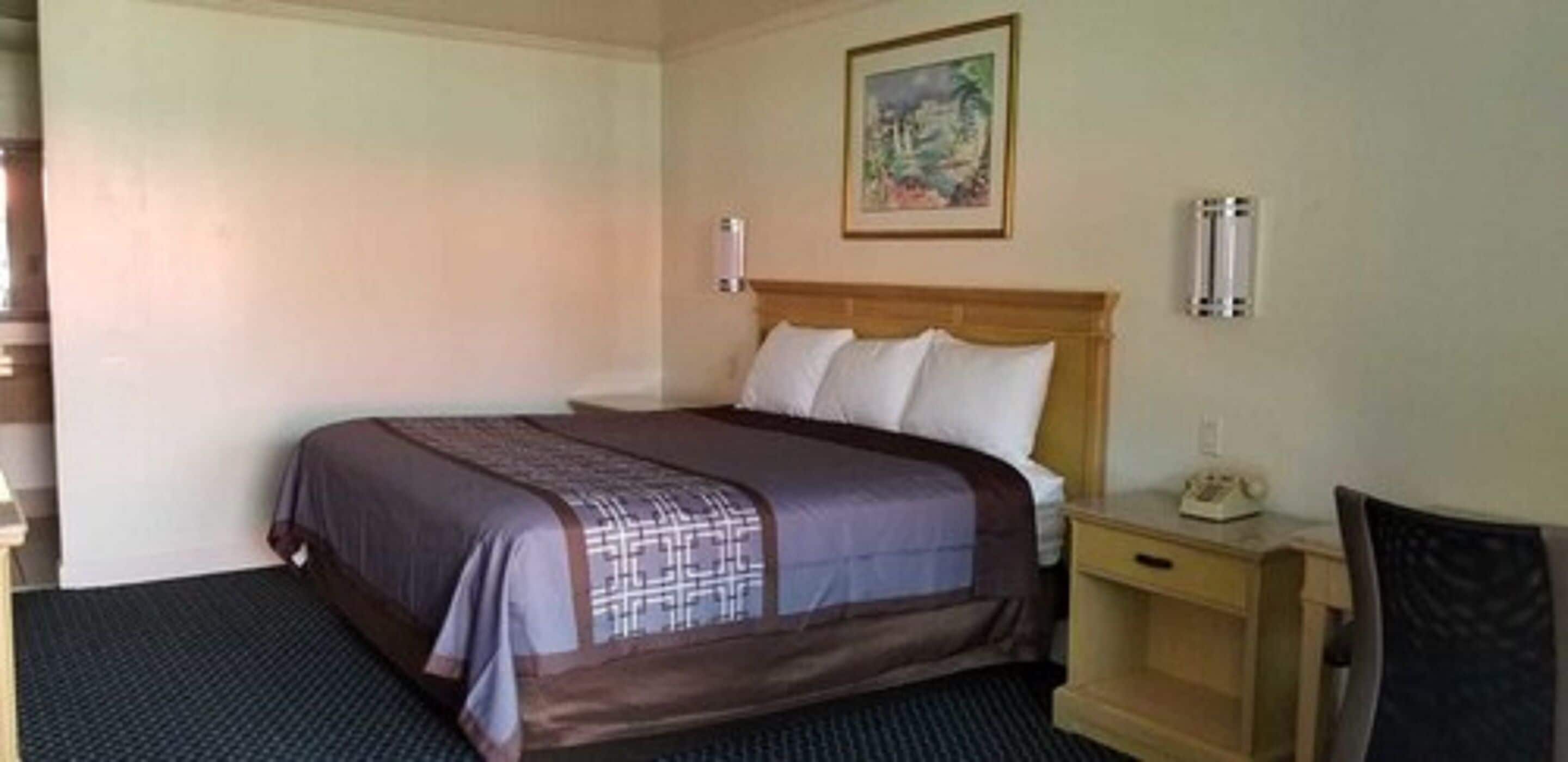 A hotel room with a bed, a nightstand, a chair, and a painting on the wall.