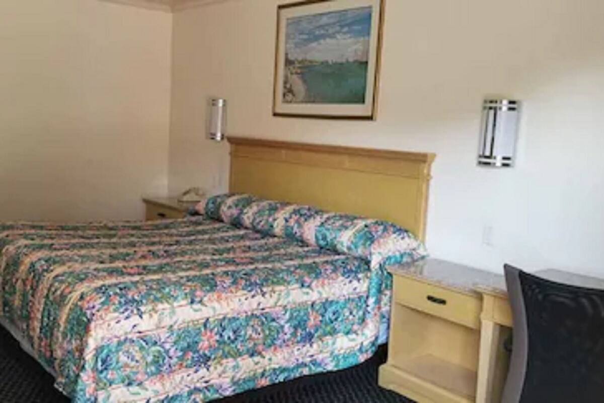 A hotel room with a bed, a desk, a chair, a nightstand, and a painting on the wall.