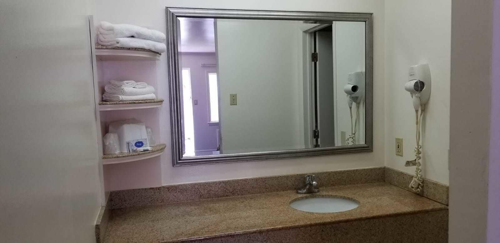 A bathroom with a large mirror, a sink, and a towel rack with folded towels.