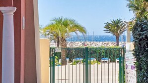 A gated entrance with a view of a pool area, palm trees, and a stone wall. - Les Rivages de Coudoulière by Interhome (Six Fours La Coudoulière)