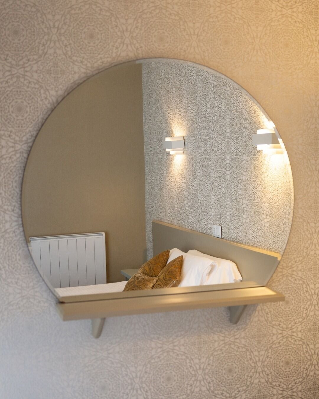 A circular mirror with a bed and wall-mounted lights.