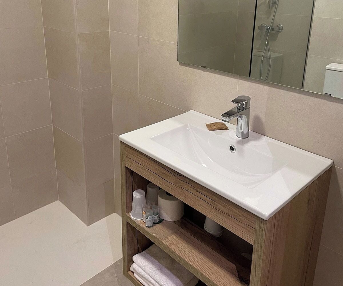 Un baño con lavamanos blanco, tocador de madera y un espejo encima.