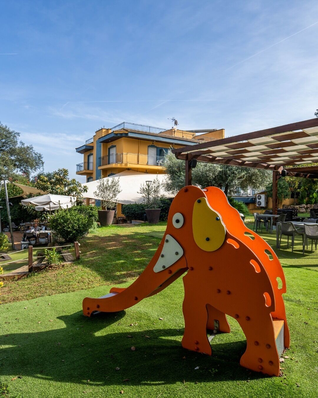 Un espacio exterior vibrante con una gran escultura de animal, un edificio con balcones y una zona de estar cubierta.