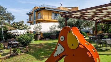 Un espacio exterior vibrante con una gran escultura de animal, un edificio con balcones y una zona de estar cubierta.