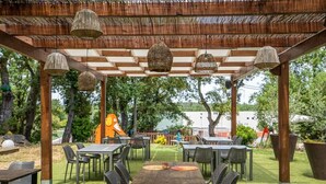 An outdoor patio with tables and chairs, a pergola with hanging lights, and a large planter. - Hostal Esteba (Caldes de Malavella)