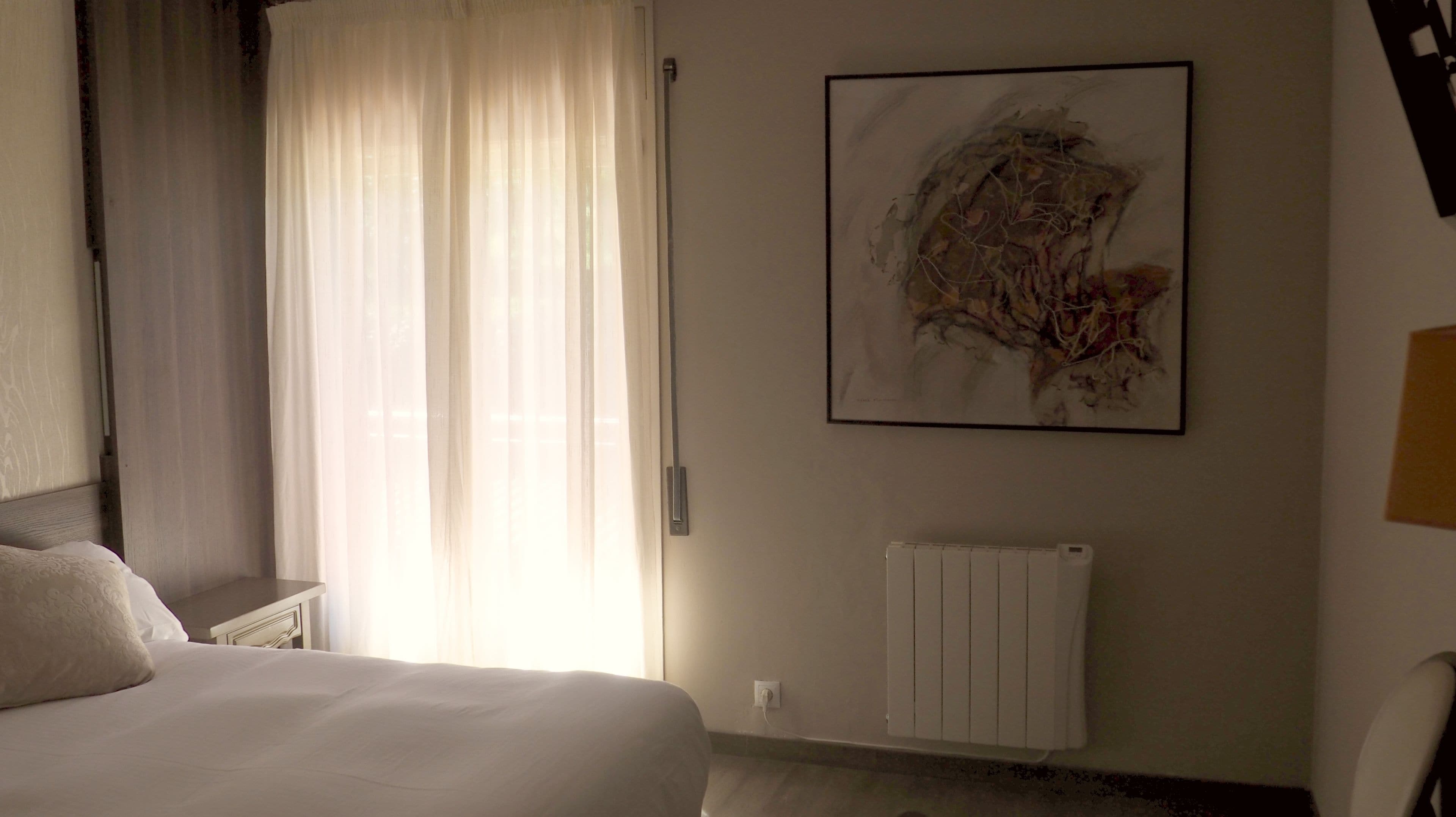 Een hotelkamer met een bed, een radiator en een groot abstract schilderij aan de muur.