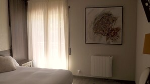 A hotel room with a bed, a radiator, and a large abstract painting on the wall.