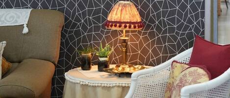 Una habitación con pared de diseño geométrico, una fotografía enmarcada, una mesa con lámpara y dos sillas.