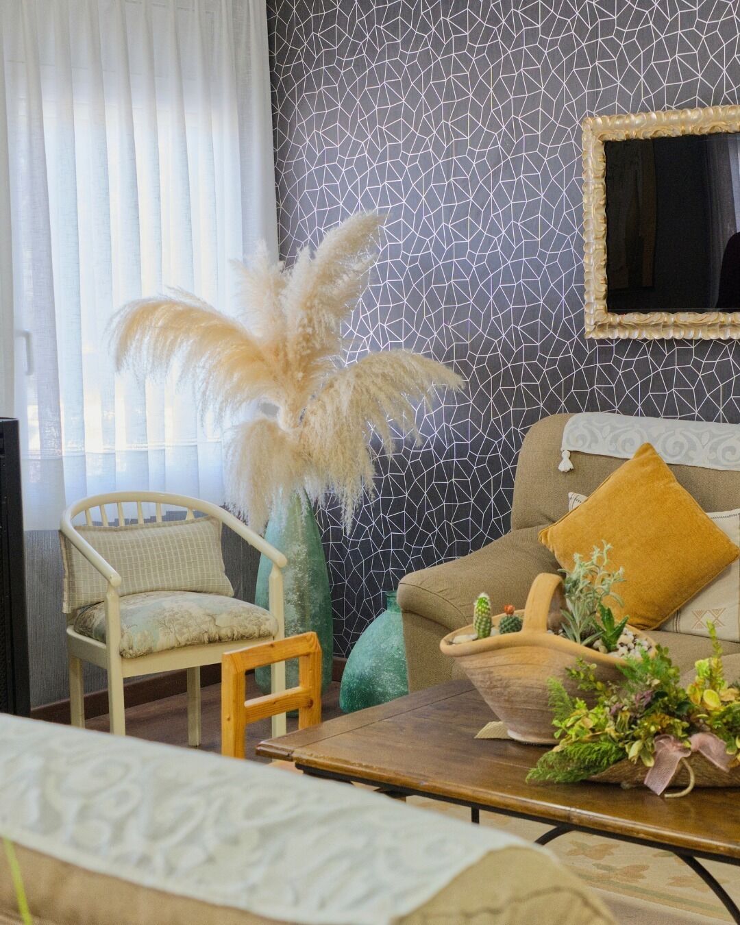 Una sala de estar con pared estampada, un sofá con cojín color mostaza, una mesa de centro de madera y una silla con almohadón.