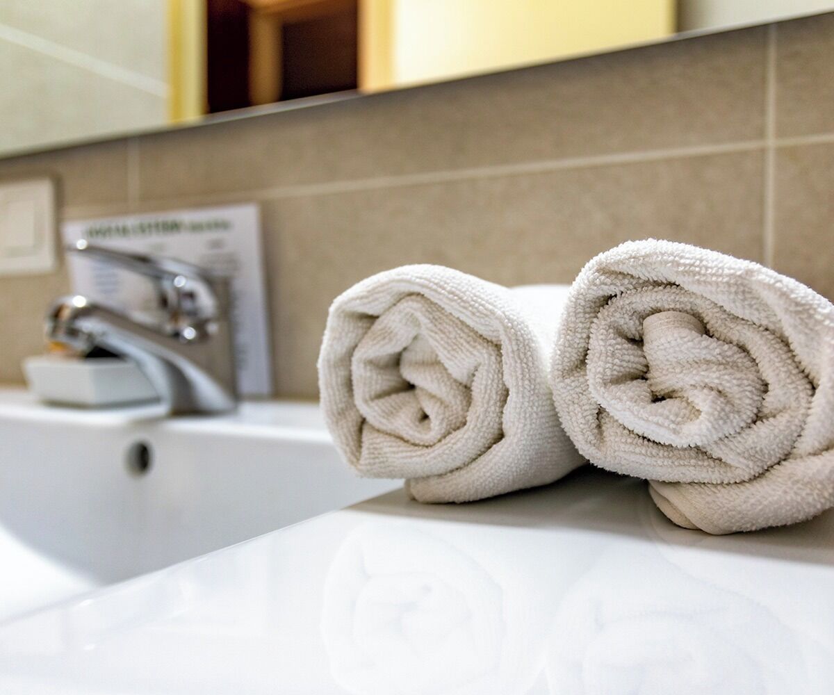 Un baño con un lavamanos blanco y dos toallas enrolladas sobre el mostrador.