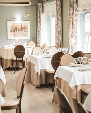 A dining area with tables set for four, each with white tablecloths and wine glasses.