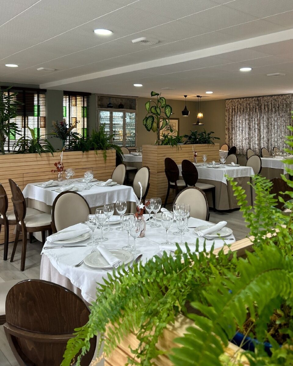 A restaurant with multiple tables set for dining, featuring a modern interior design with plants and neutral color tones.
