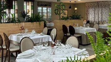 A restaurant with multiple tables set for dining, featuring a modern interior design with plants and neutral color tones.