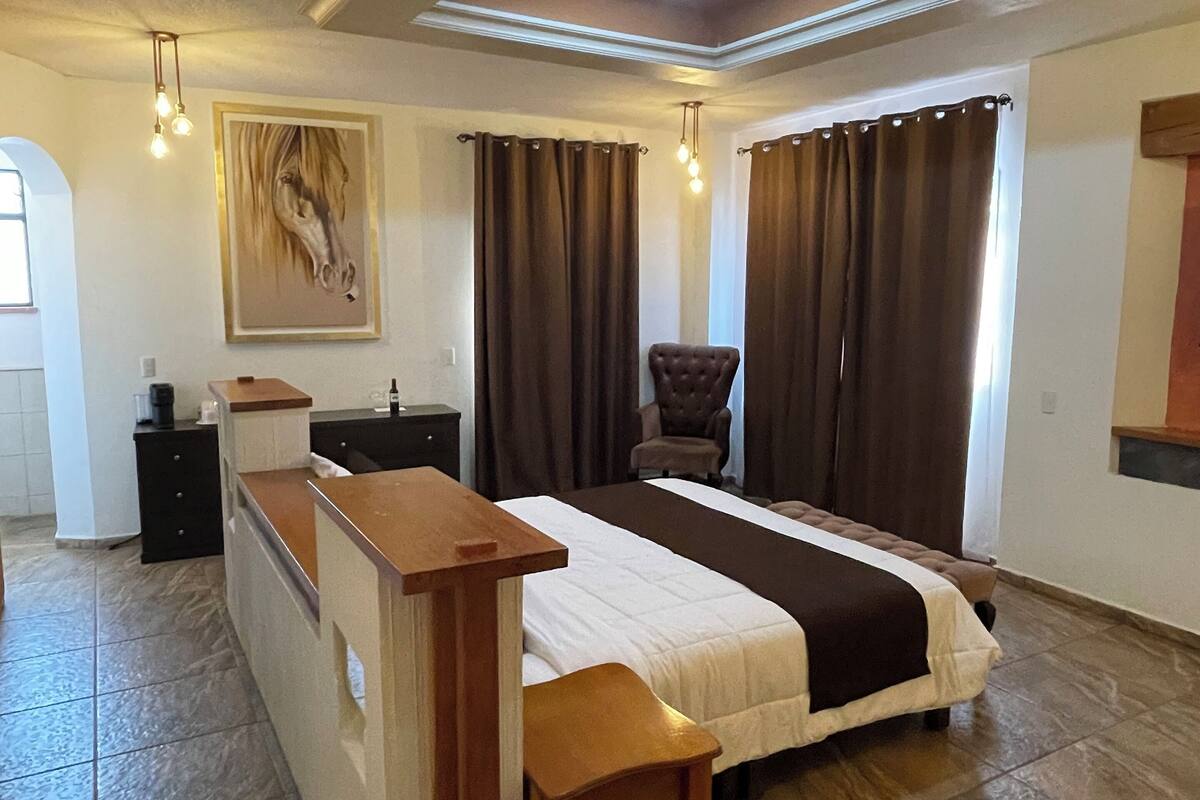A spacious bedroom with a large bed, a wooden bench, a desk, and a chair.