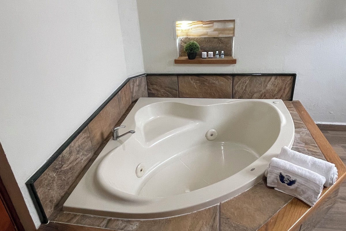 A corner bathroom with a freestanding bathtub, a wooden bench, and a small shelf with a plant and toiletries.