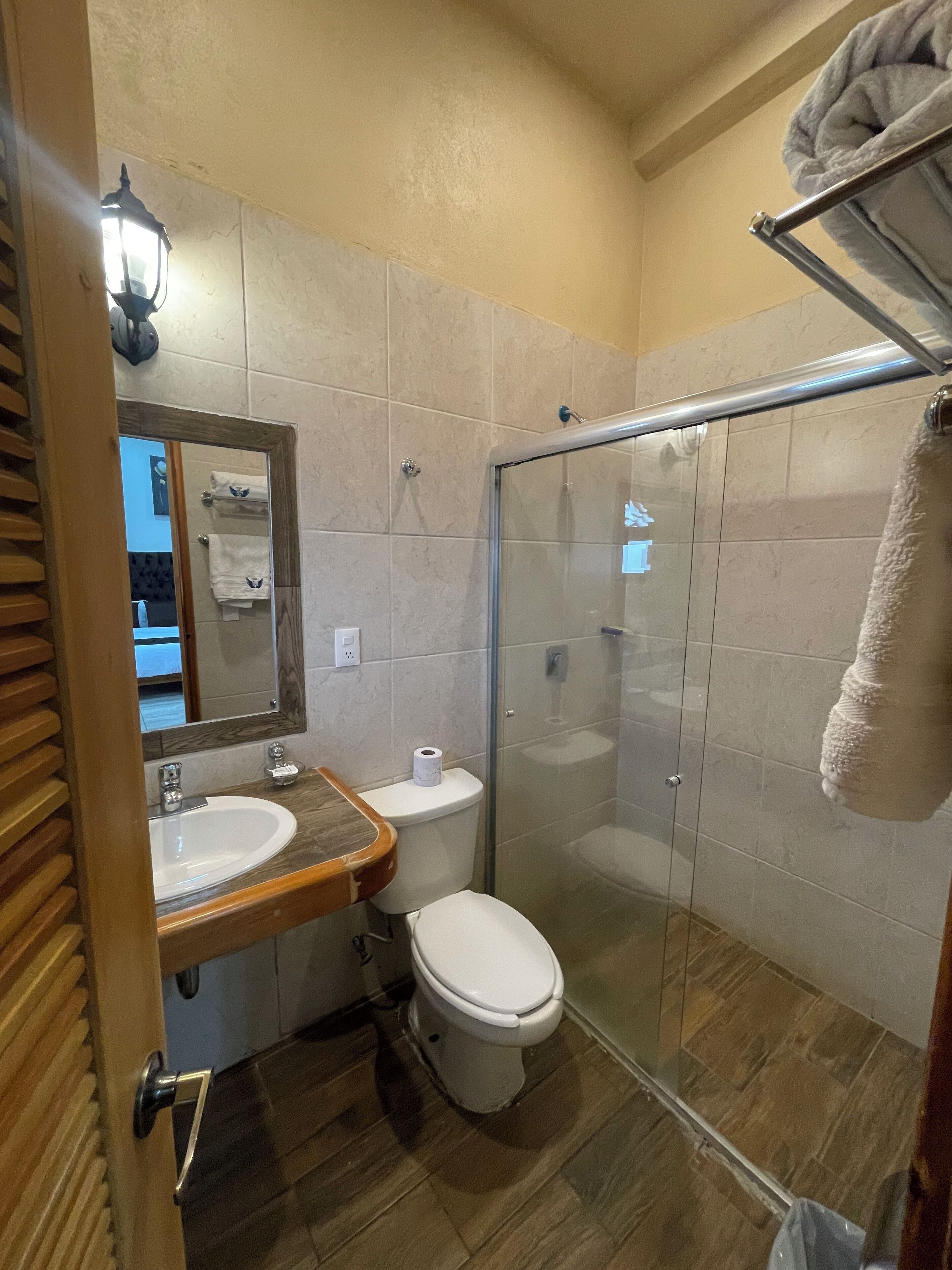 A bathroom with a wooden vanity, a white toilet, a glass shower enclosure, and a towel rack.
