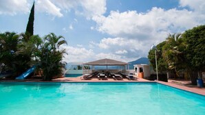Una piscina con sillones de descanso, una zona de estar techada y palmeras.