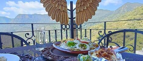 Una mesa de comedor con diversos platos, como un bistec, ensalada y otras comidas, con un paisaje montañoso de fondo.
