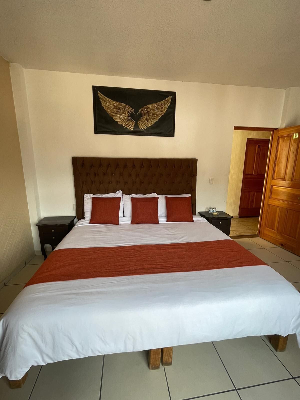 A large bed with a brown headboard, white bedding, and red accents.