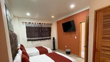 A hotel room with two beds, a television on the wall, and a door.