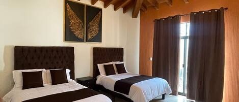 Habitación de hotel con dos camas, techo de madera y un ventanal grande con cortinas.