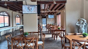 Un restaurante con mesas y sillas de madera, paredes de piedra y lámparas colgantes.