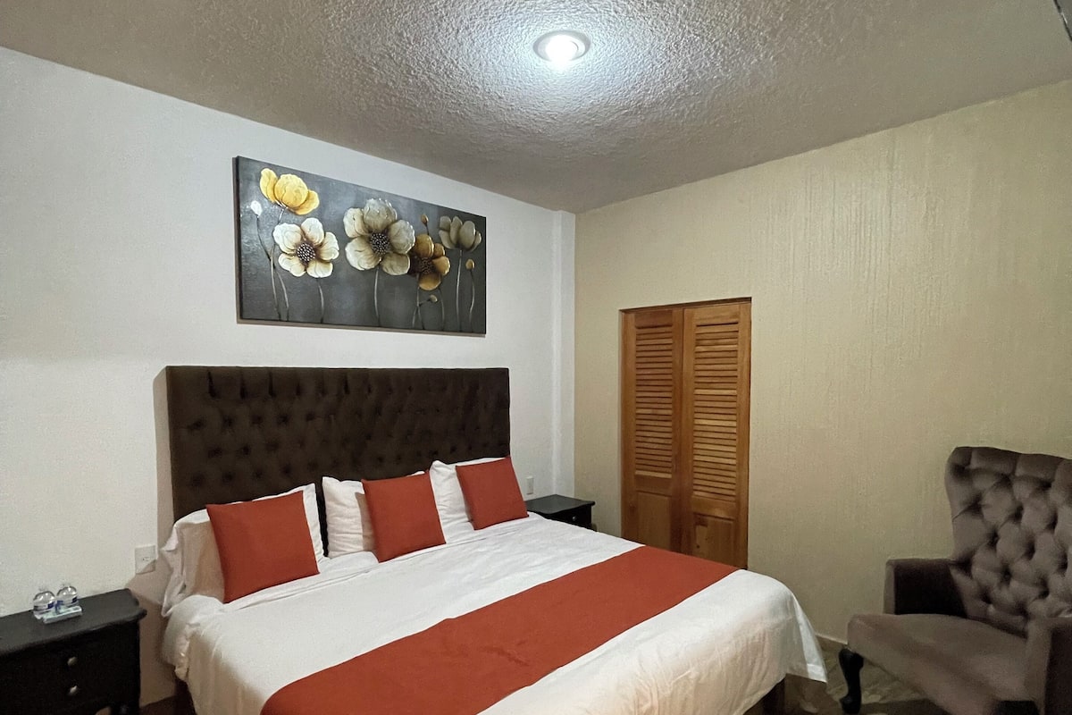 A bedroom with a large bed, a headboard, a nightstand, a wooden door, and a chair.
