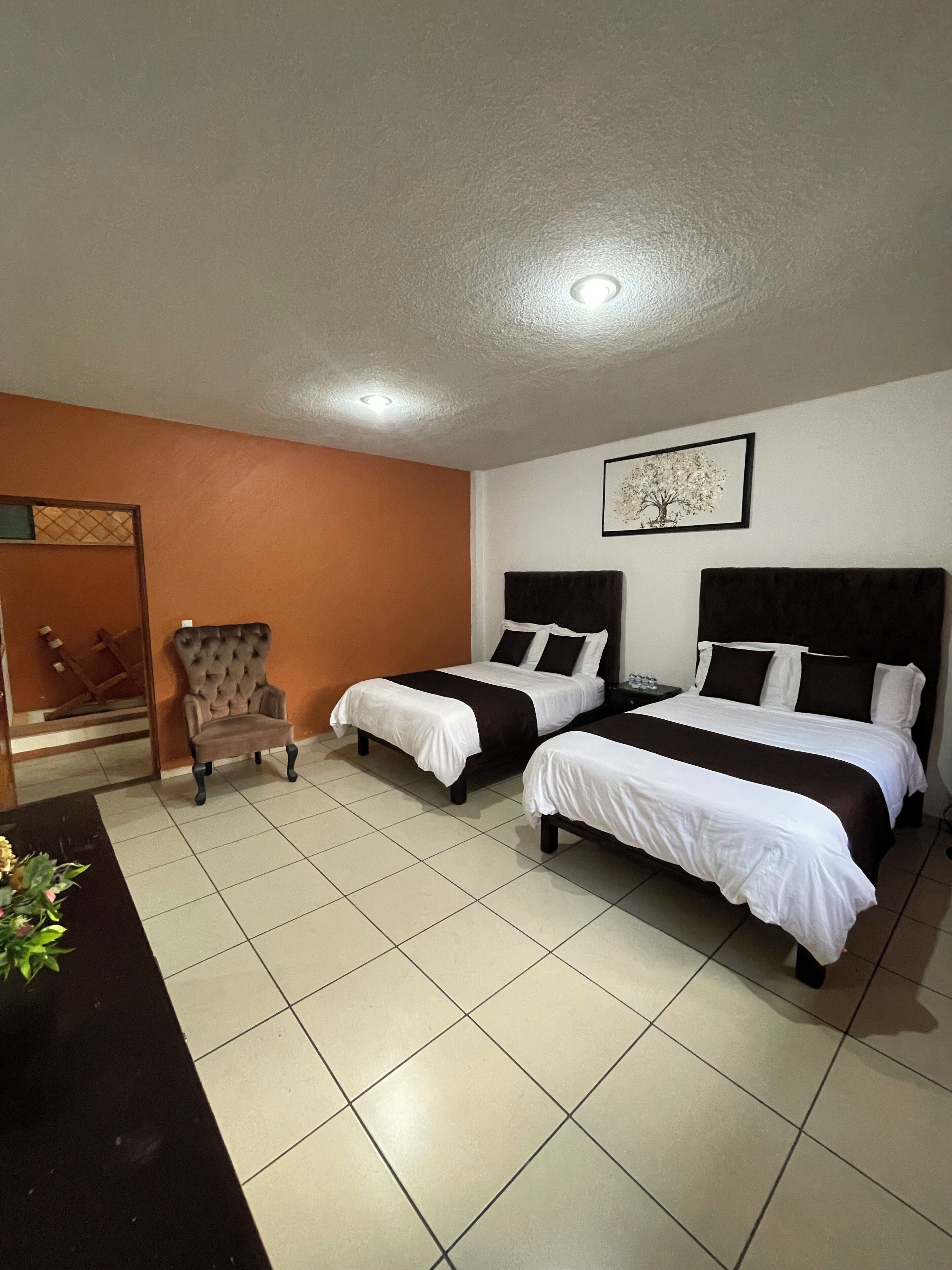 A hotel room with two beds, a chair, and a small table.