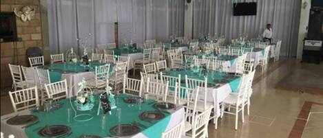 A banquet hall with multiple round tables covered in white tablecloths and teal table runners, surrounded by white chairs.