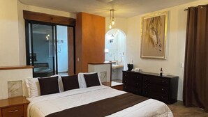 Habitación de hotel con una cama grande, un banco, un aparador, un espejo y un cuadro en la pared.