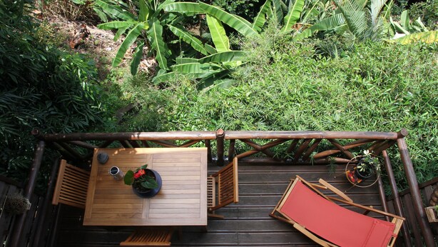 Une terrasse en bois avec une table et des chaises, entourée d’une végétation luxuriante.