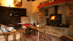 A cozy room with a stone fireplace, a wooden table with a bottle of wine, and a comfortable chair. - 3 houses with 6x3 beds, approx. 1 hectare of land and a swimming pool. (Ploërdut)