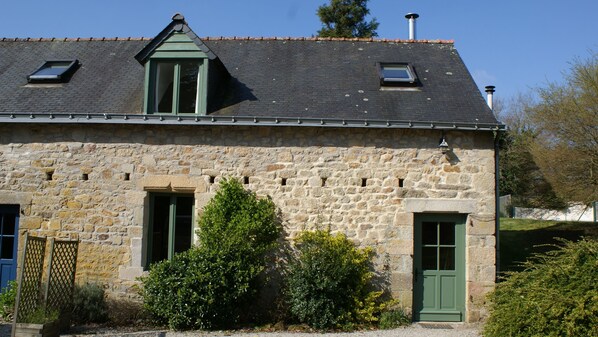 A stone building with a gabled roof, two windows with shutters, and a green door.