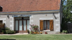 A two-story building with a tiled roof, a front entrance with a wooden door, and a small garden area with potted plants and flowers. - Lodging near Amboise, Chenonceau, Chaumont / Loire  (Mosnes)